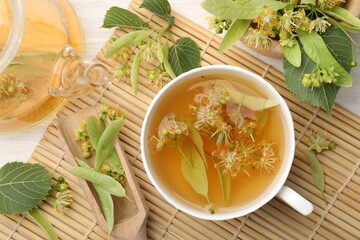 Fresh linden tea in cup, teapot and flowers on white wooden table, flat lay