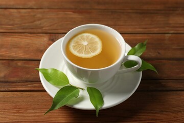 Tasty green tea with lemon in cup and leaves on wooden table, above view