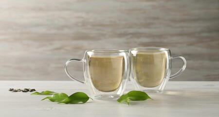 Tasty green tea in glass cups, brew and leaves on light wooden table