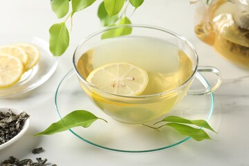 Refreshing green tea with lemon and leaves on white marble table, closeup