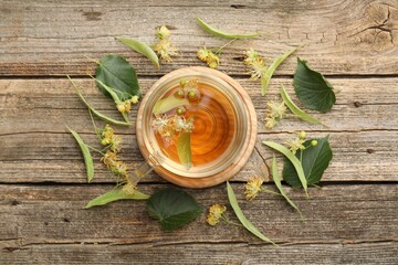 Tasty linden tea in cup, leaves and flowers on wooden table, flat lay