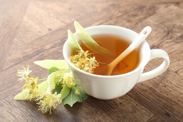 Tasty linden tea in cup, leaves and flowers on wooden table, closeup