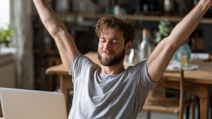 A young man celebrates a successful accomplishment while working from home, radiating joy and satisfaction.