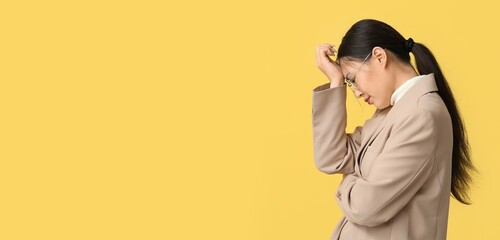 Young Asian businesswoman suffering from headache on yellow background with space for text
