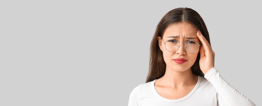 Young Asian woman suffering from headache on grey background with space for text