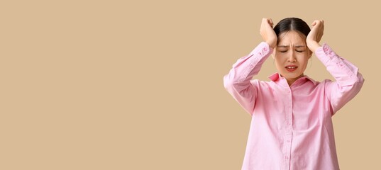 Young Asian woman suffering from headache on beige background with space for text