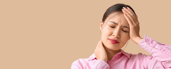 Young Asian woman suffering from headache on beige background with space for text