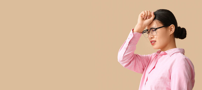 Young Asian woman suffering from headache on beige background. Brain Injury Awareness Month