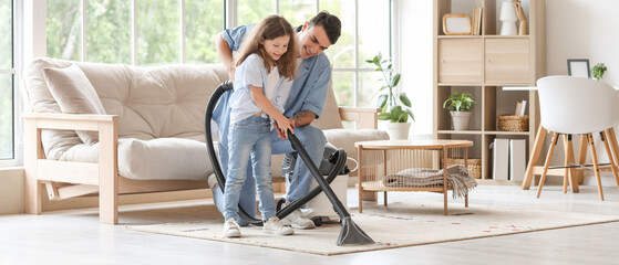 Young father and his daughter with vacuum cleaner cleaning carpet together at home