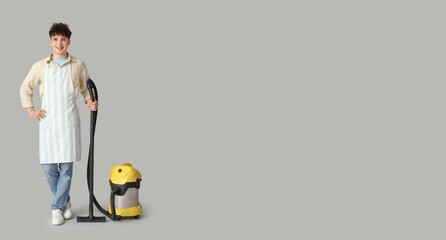 Young man with vacuum cleaner on grey background with space for text