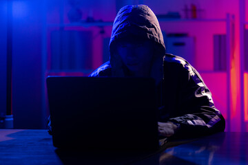 Young Man in Hoodie Working on Laptop in Dark Tech Environment