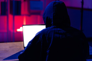 Young Man in Hoodie Working on Laptop in Dark Tech Environment