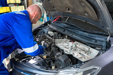 Male Caucasian auto mechanic in workwear jumpsuit working in auto repair shop fixing car 