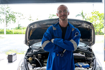 Male Caucasian auto mechanic in workwear jumpsuit standing arm cross  in auto repair shop 