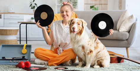 Young woman with vinyl disks for record player and Australian Shepherd dog sitting on carpet at home