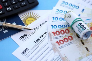 Argentine pesos money bills in big amount lies on table with pen, calculator, passport and tax forms