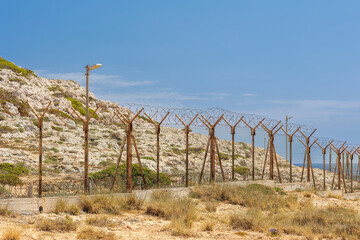Barbed Wire Border Fence in Arid Landscape, Rusty metal fence topped with barbed wire stretching...