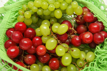 Mesh bag with different fresh grapes on white background, closeup