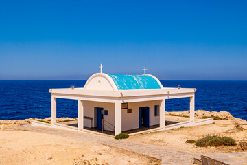 Fototapeta premium Seaside Chapel with Blue Dome and Ocean View in Cyprus,small white chapel with a light blue dome and crosses, perched on a rocky coastline in Cyprus with the Mediterranean ,summer travel , hot summer 