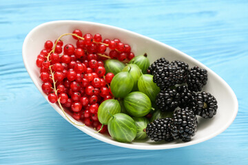 Bowl with fresh blackberry, gooseberry and currant on blue wooden background, closeup