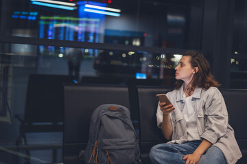 Female passenger waiting for flight at airport at night lounge and using smart phone