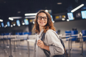 Young cute woman traveler in glasses standing at check-in counters at airport at night