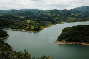 Panoramic view of winding shoreline of Rovni Lake with villages and hills in spring, Valjevo, Serbia