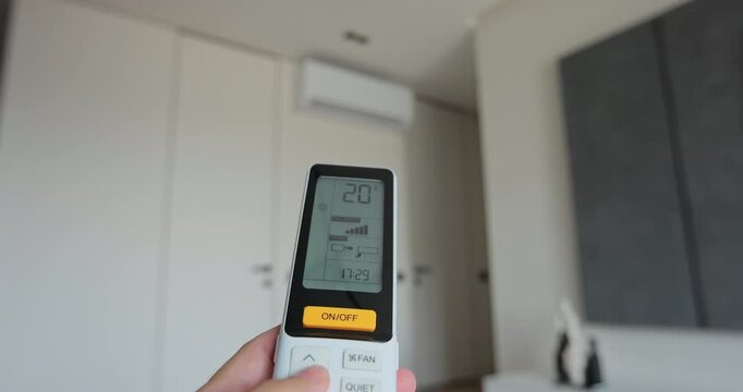 Man adjust the temperature on air conditioner in the living room. Hand uses air conditioner remote control.