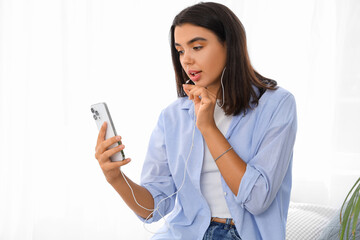 Naklejka premium Young woman in earphones using mobile phone at home