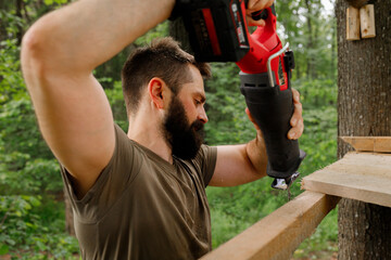 brutal young brunette man, dad with beard is nailing building a tree house to his little son with...