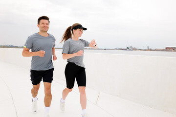 Couple enjoying a refreshing morning jog along the waterfront promenade under an overcast sky