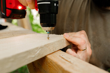young brunette man, dad screwing a screw into a wooden plank with a professional red drill,...