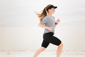 Energetic woman sprinting on a bright day, showcasing determination and strength in an urban...