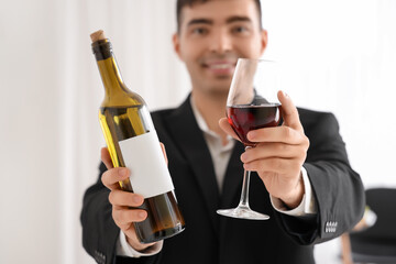Young sommelier with bottle and glass of red wine in kitchen, closeup