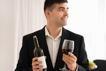 Young sommelier with bottle and glass of red wine in kitchen, closeup