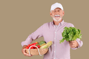 Mature male farmer with wicker basket full of different ripe vegetables on green background