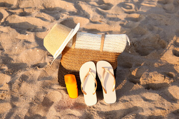 Stylish beach bag, hat, flip-flops and sunscreen cream on sand