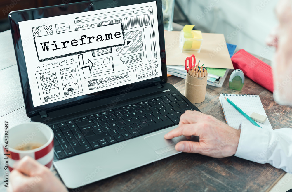 Wall mural creative professional designs a wireframe layout on a laptop while enjoying coffee at a workspace