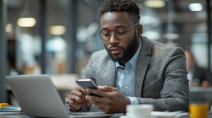 Serious african american professional using smartphone in modern office setting working with laptop