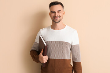Happy young man with book on beige background