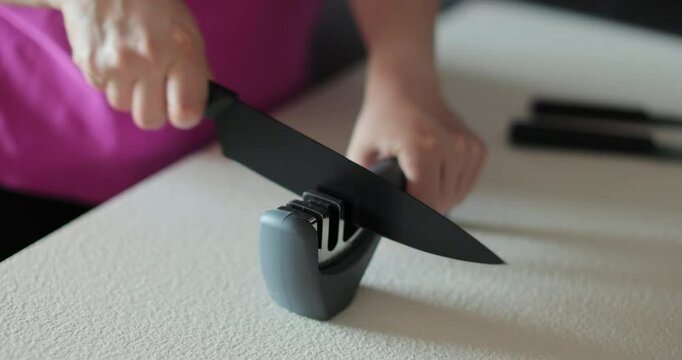 Close-up of woman sharpening knife with knife sharpener on the kitchen table. Knife sharpening.
