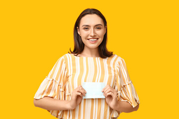 Beautiful young woman with menstrual pad on yellow background