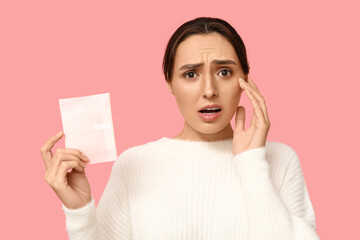 Beautiful displeased woman with menstrual pad on pink background