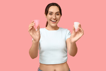 Beautiful young woman with menstrual cups on pink background