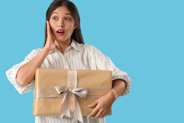Beautiful shocked Asian woman with gift box on blue background