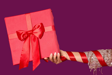 Female hand with gift box on purple background