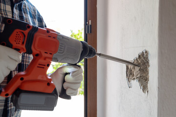 Carpenter electrician with demolition hammer prepares the cavity in the wall where to insert the...