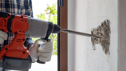 Carpenter electrician with demolition hammer prepares the cavity in the wall where to insert the...