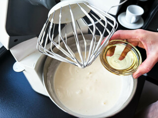 Making dough in a planetary mixer. Women's hands pour oil into a bowl with dough. Cooking at home.