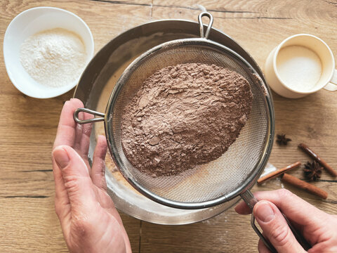The process of making a homemade pie. The girl's hands sift cocoa powder into a bowl. Homemade baking.
